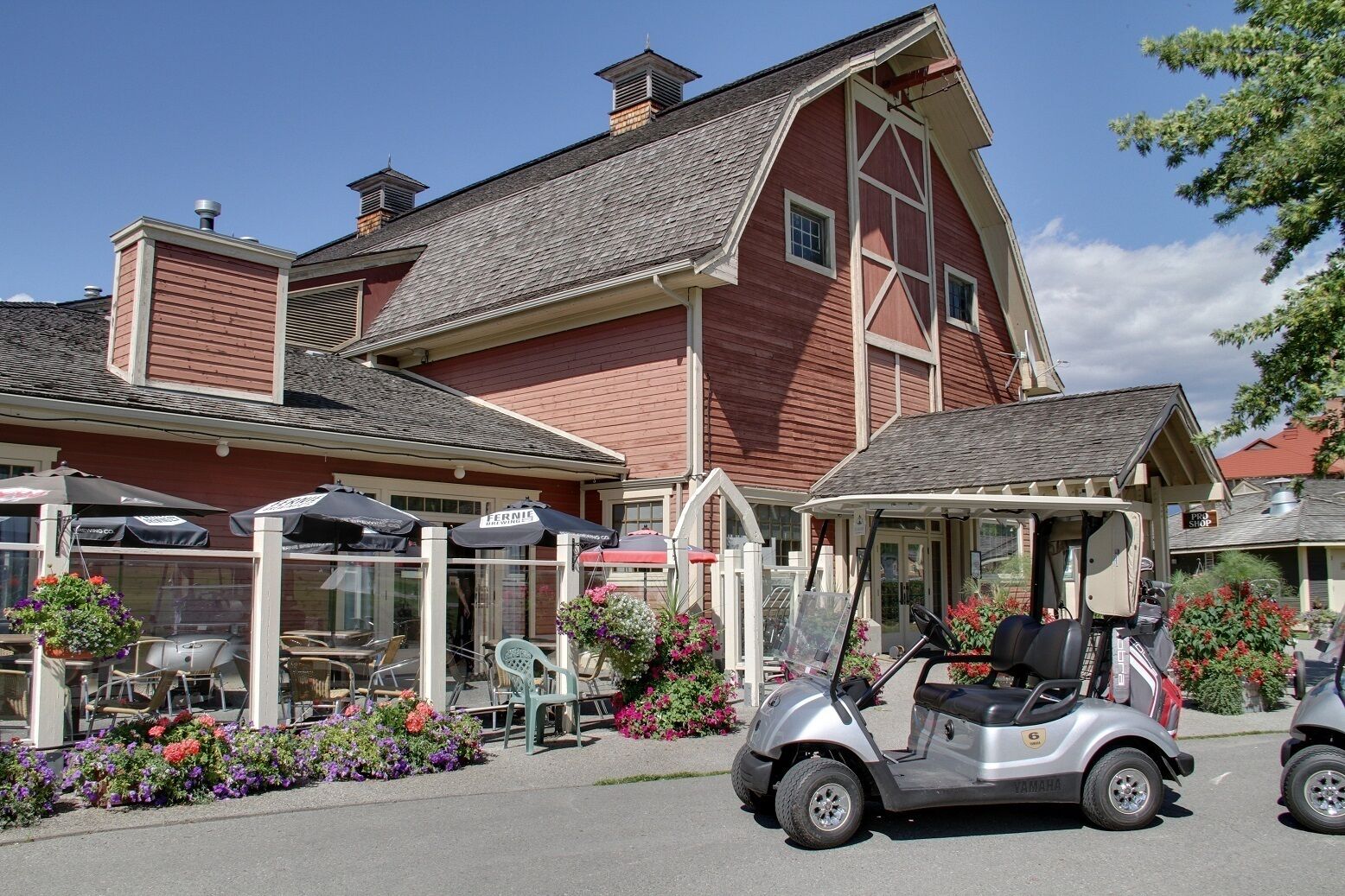 Een roodbruin schuurachtig gebouw met een overdekt terras en een golfkarretje ervoor geparkeerd.