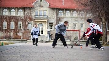 A group of people playing hockey on an outdoor court with a stone building in the background.