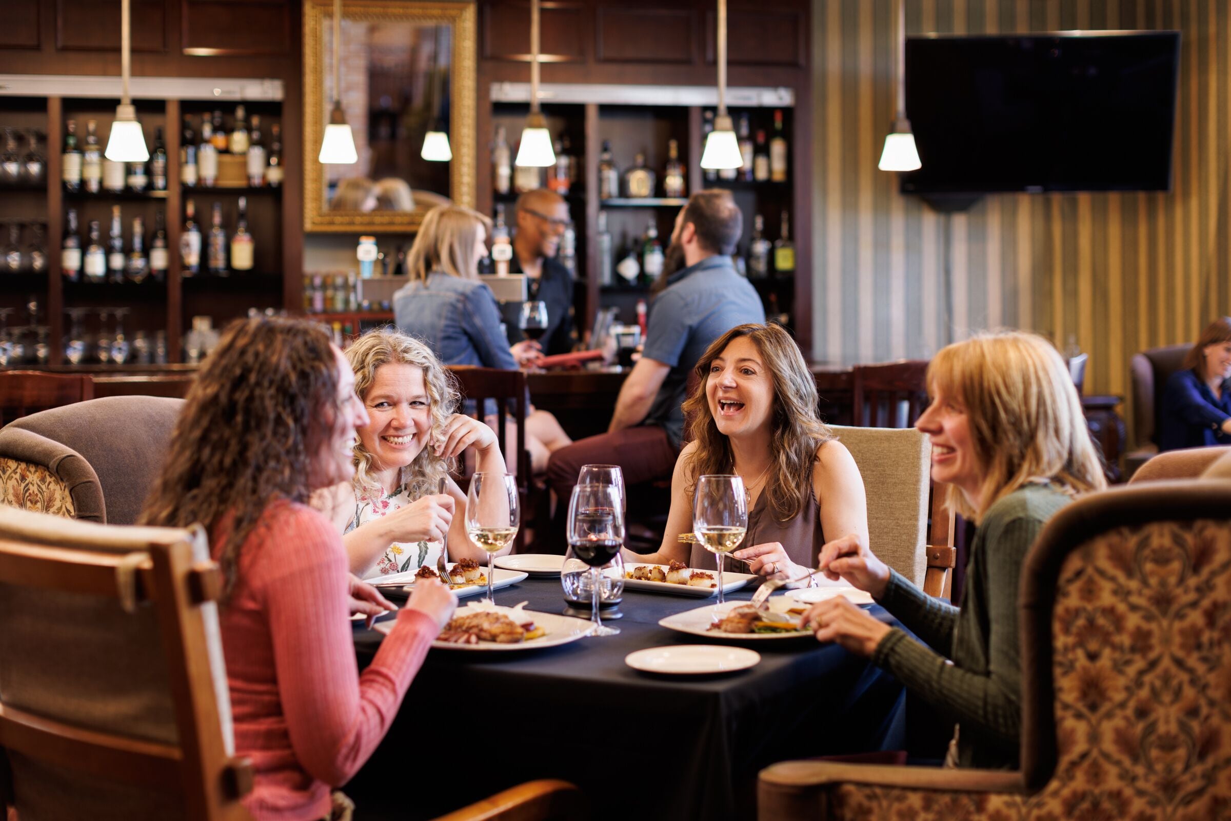Een groep mensen aan het dineren in een restaurant, met een bar op de achtergrond.