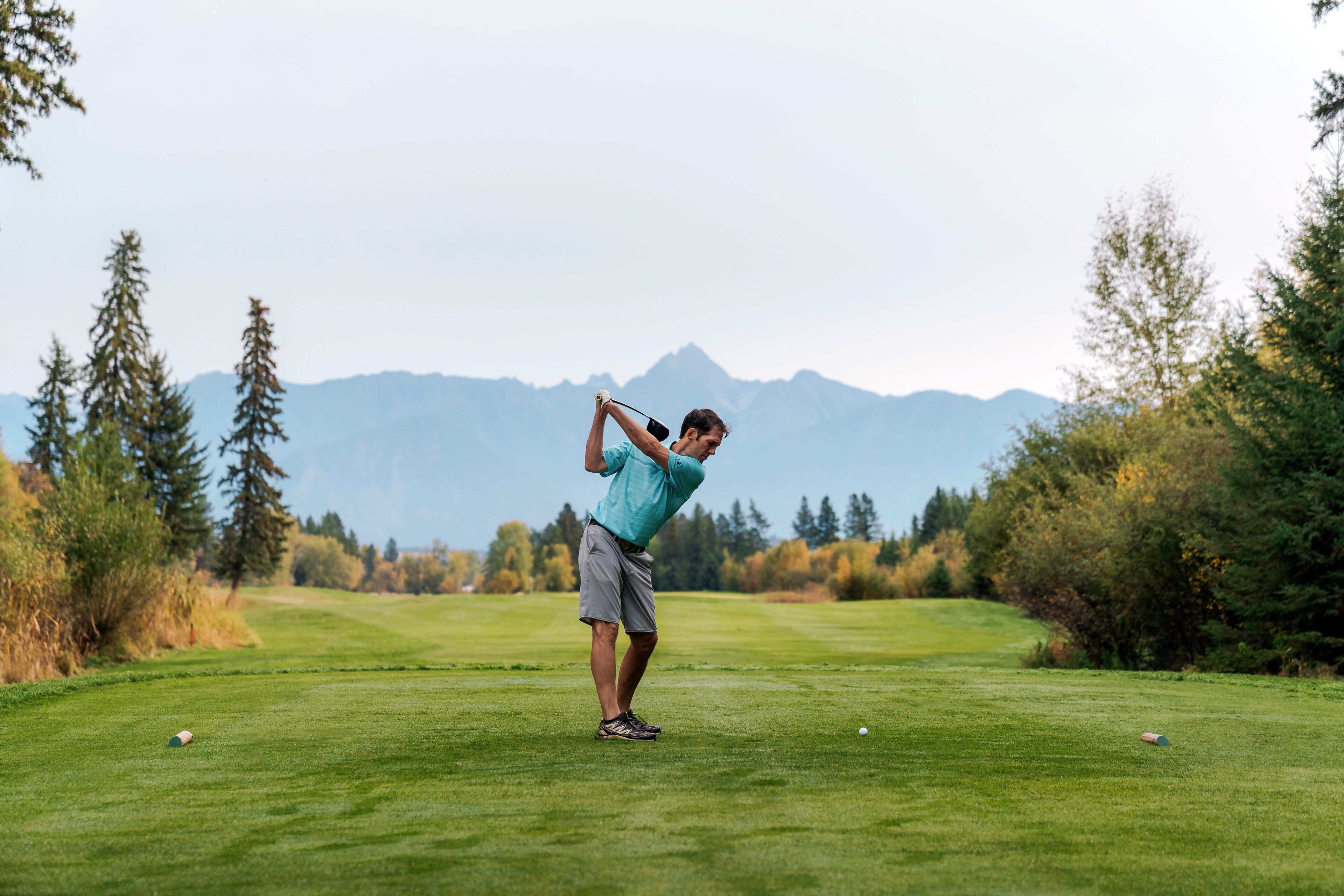 Una persona su un campo da golf con montagne sullo sfondo.