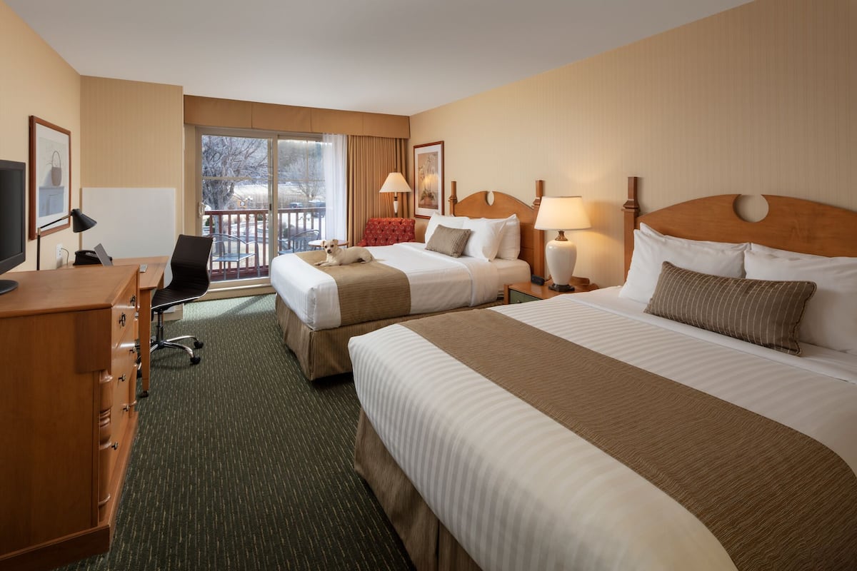 A hotel room with two beds, a desk, a chair, a TV, and a balcony with a view.