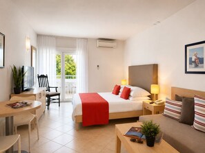 Ein Hotelzimmer mit Bett, Nachttisch, Lampe, Stuhl und Blick auf Grün.