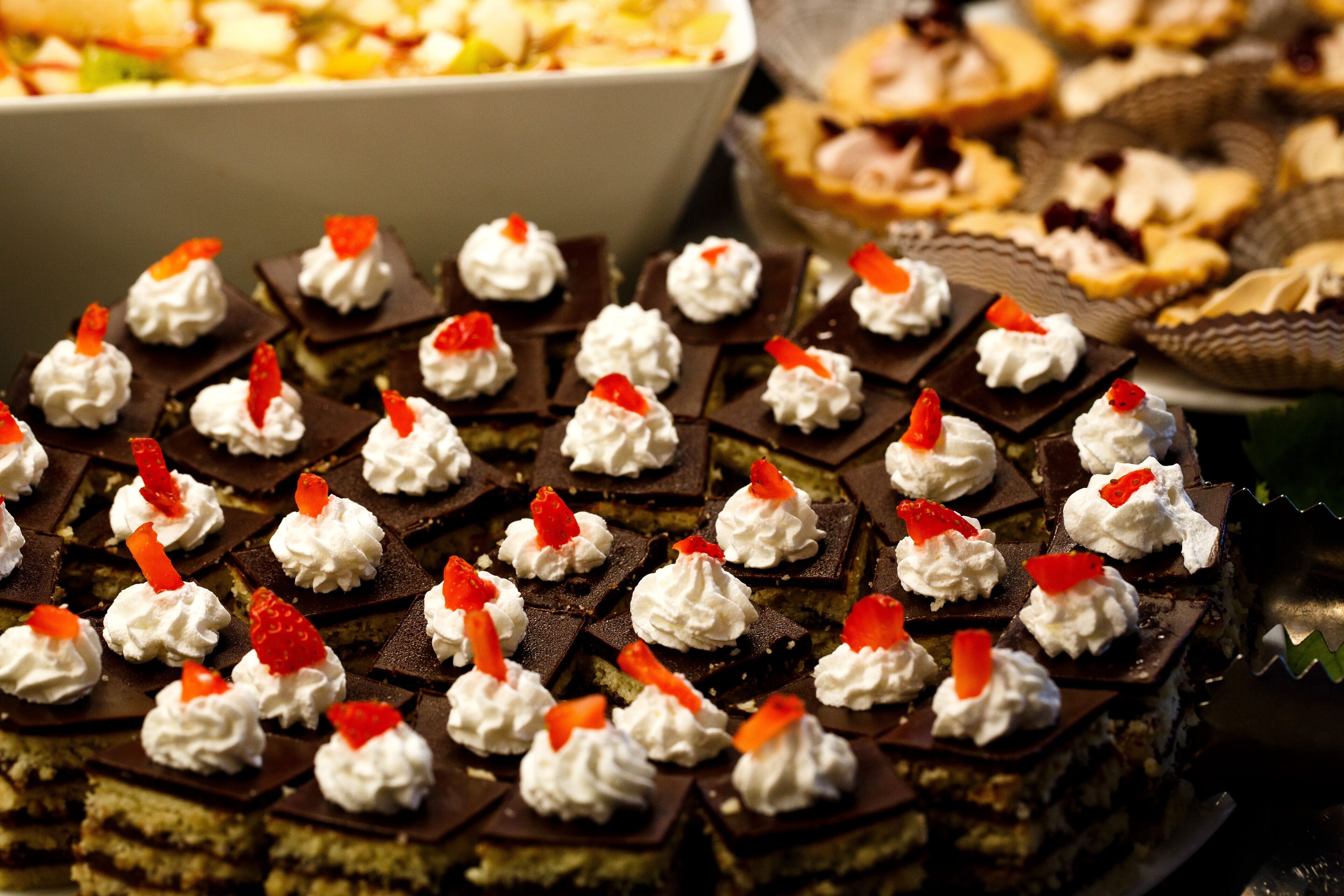 Un assortiment de desserts, notamment des carrés de chocolat accompagnés de crème fouettée et de fraises.