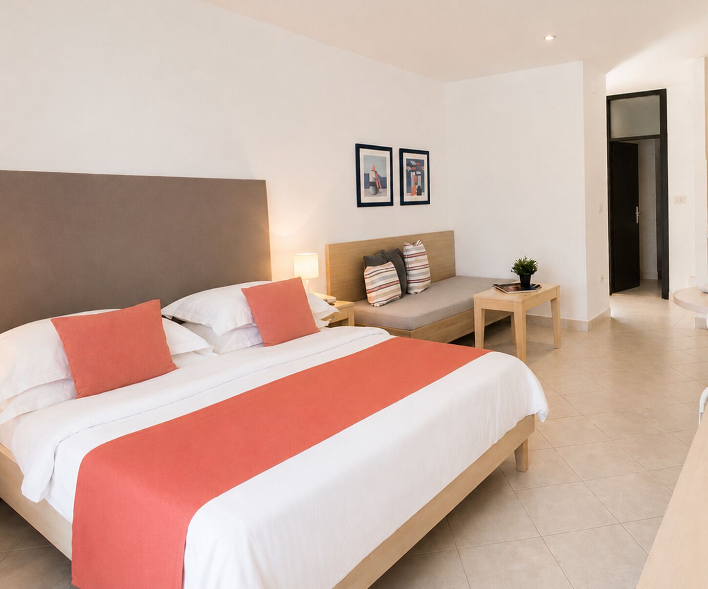 A hotel room with a bed, a nightstand, a sofa, and a small table with a plant.