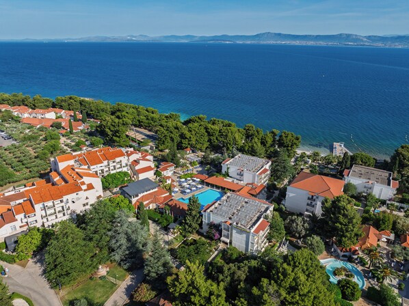 Eine Vogelperspektive eines Küstenresorts mit mehreren Gebäuden, einem Schwimmbad und Blick auf das Meer.