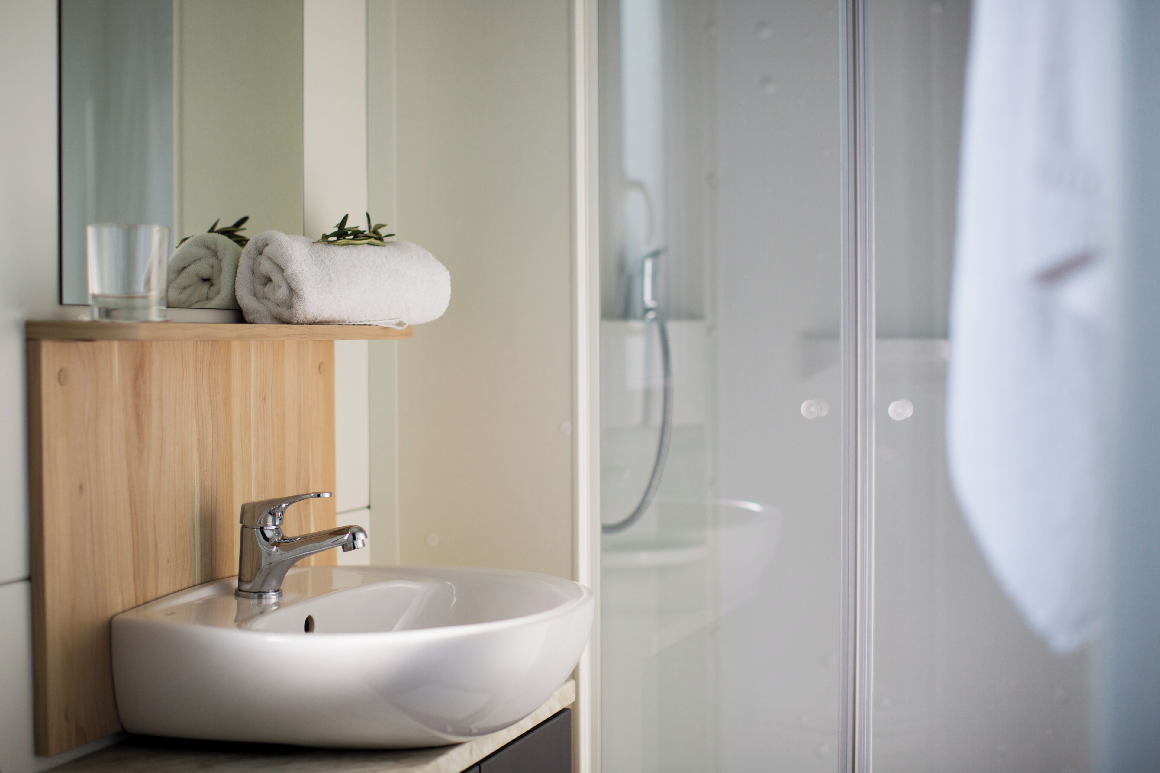 Un baño con tocador de madera, un lavabo blanco y cabina de ducha con paredes de vidrio.