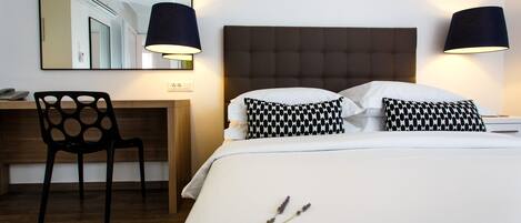 A hotel room with a bed, two black lamps, a desk with a chair, and a mirror on the wall.