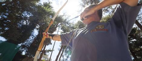 A person holding a bow and arrow outdoors with trees in the background.