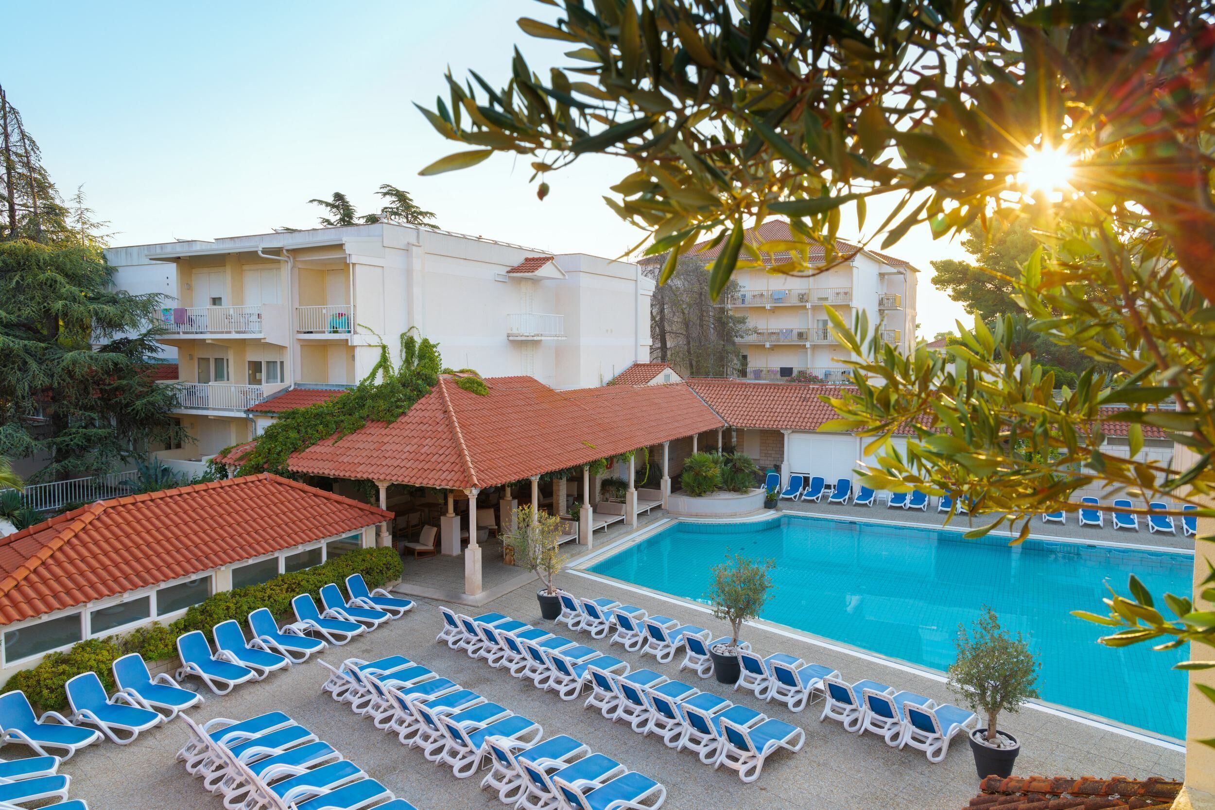 A hotel with a swimming pool, sun loungers, and a covered area with umbrellas.