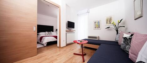 A modern bedroom with a bed, a TV, a small table, and a sofa.