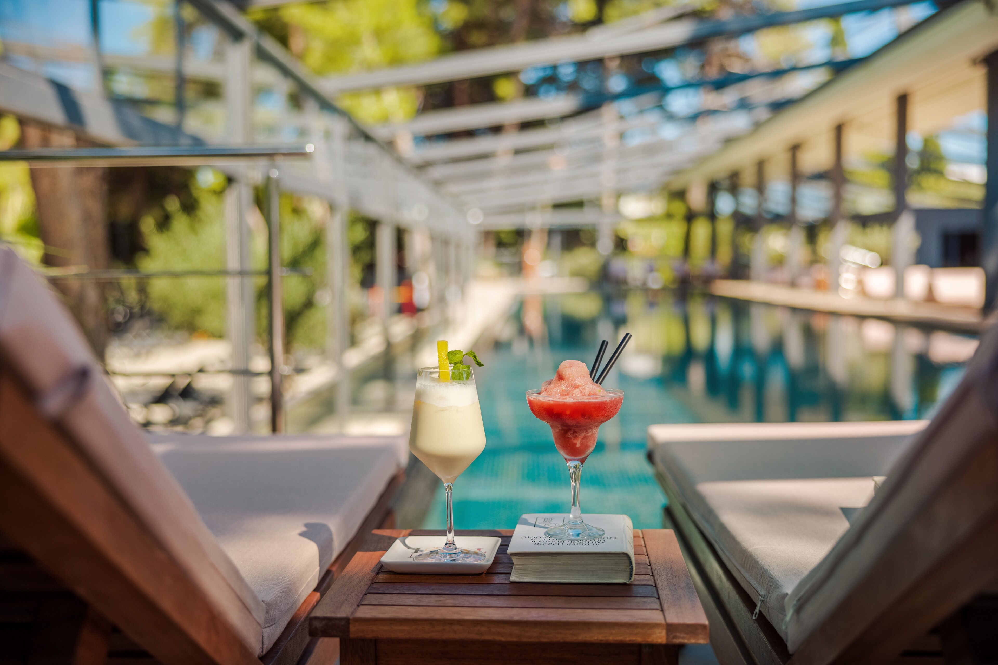 A poolside view with lounge chairs and two drinks on a wooden table.