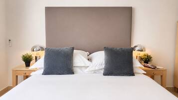 Una cama bien tendida con un cabecero grande, dos mesitas de noche con lámparas, y una pequeña planta en cada mesita.