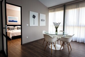 Ein modernes Hotelzimmer mit einem Bett, einem Glastisch mit weißen Stühlen und zwei gerahmten Bildern an der Wand.