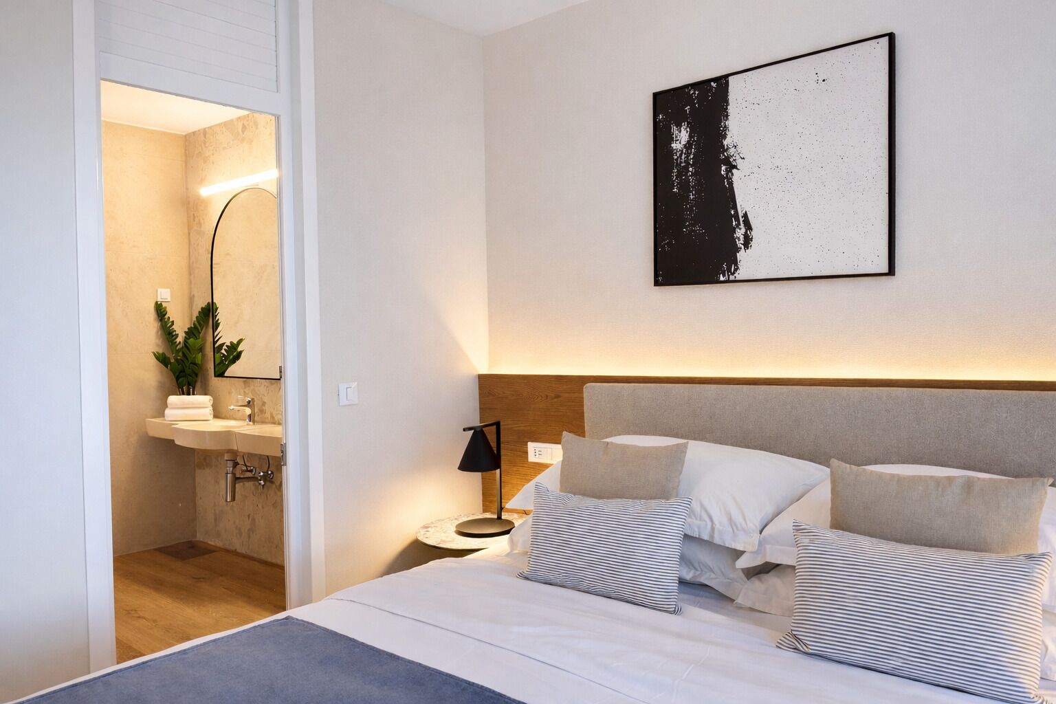 A modern hotel room with a bed, bedside table, lamp, and a framed artwork on the wall.