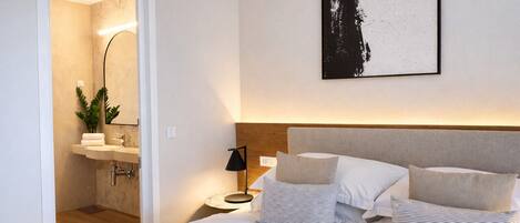 A modern hotel room with a bed, bedside table, lamp, and a framed artwork on the wall.