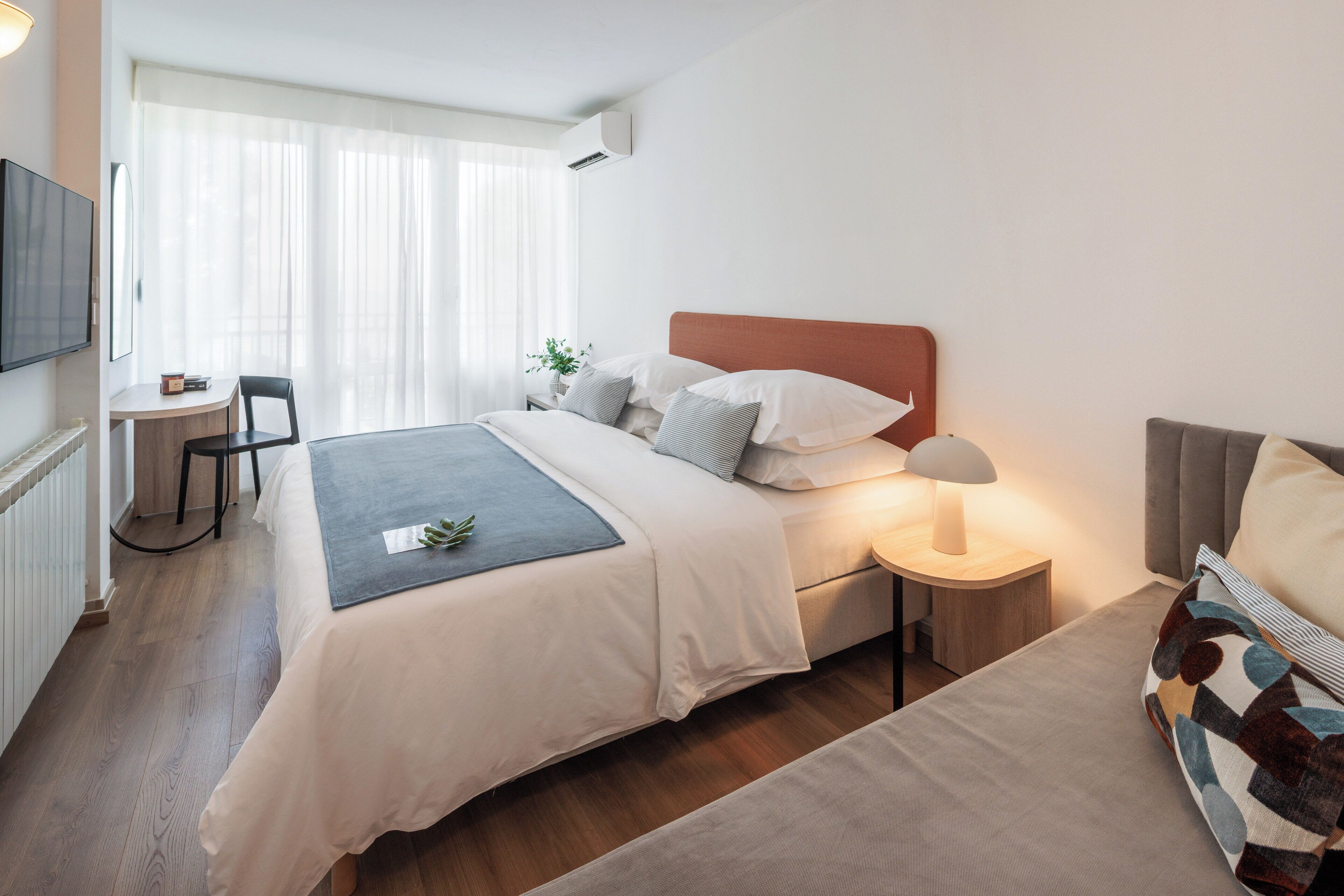 A modern hotel room with a large bed, bedside tables, a desk, and a TV.