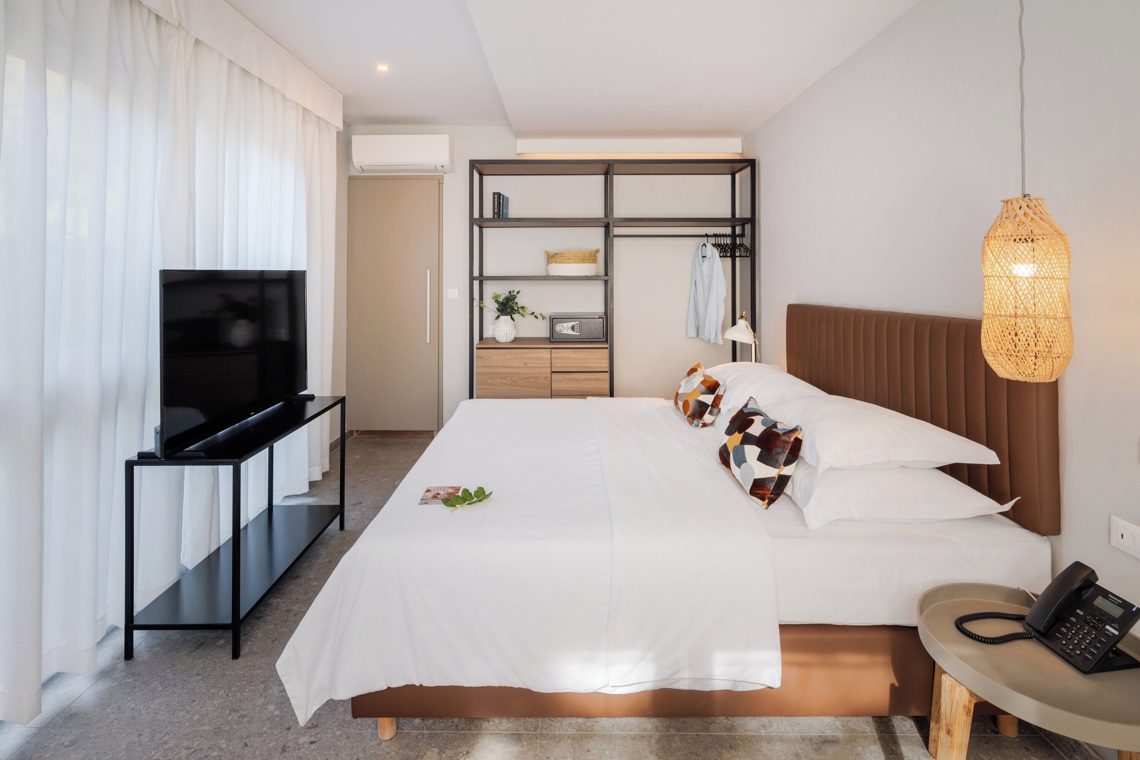 Une chambre d’hôtel moderne équipée d’un grand lit, d’une télévision, d’une armoire et d’une table de chevet avec un téléphone.