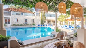 A poolside area with lounge chairs, a pool, and a view of a building with a tiled roof. - Waterman Svpetrvs Resort (Supetar)