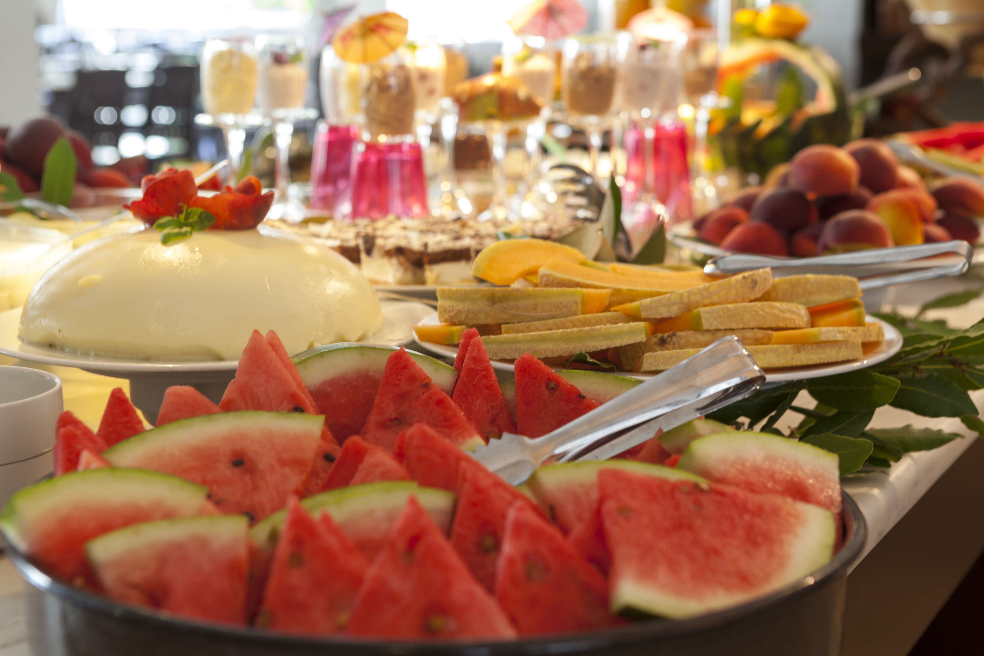 Buffet com diversas opções de comida, incluindo fatias de melancia, frutas e sobremesas.