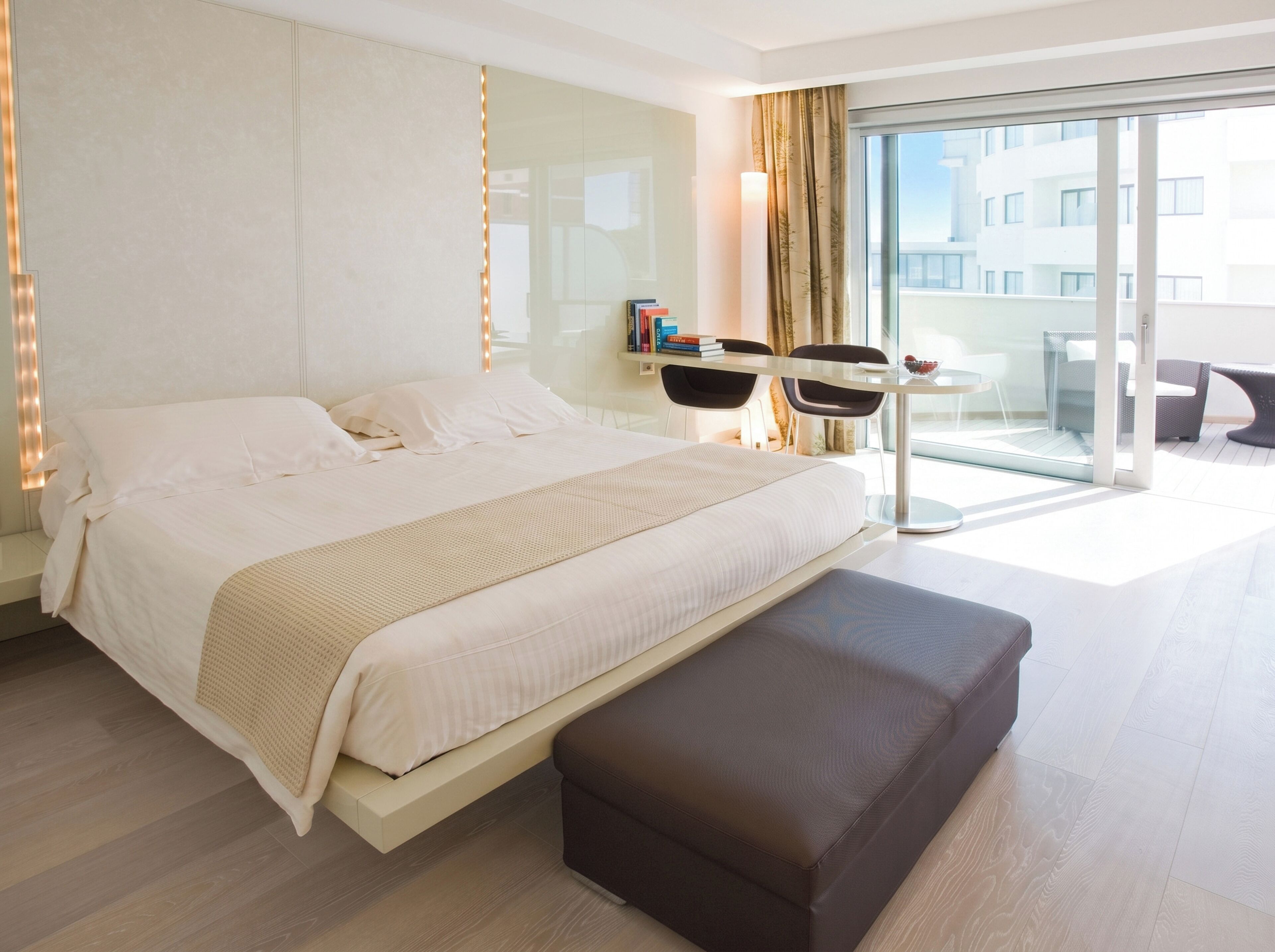 A modern hotel room with a large bed, a small table, and a balcony with seating.