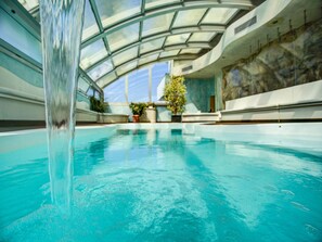 An indoor swimming pool with a glass ceiling, potted plants, and a stone wall. - Hotel Premier & Suites (Cervia)