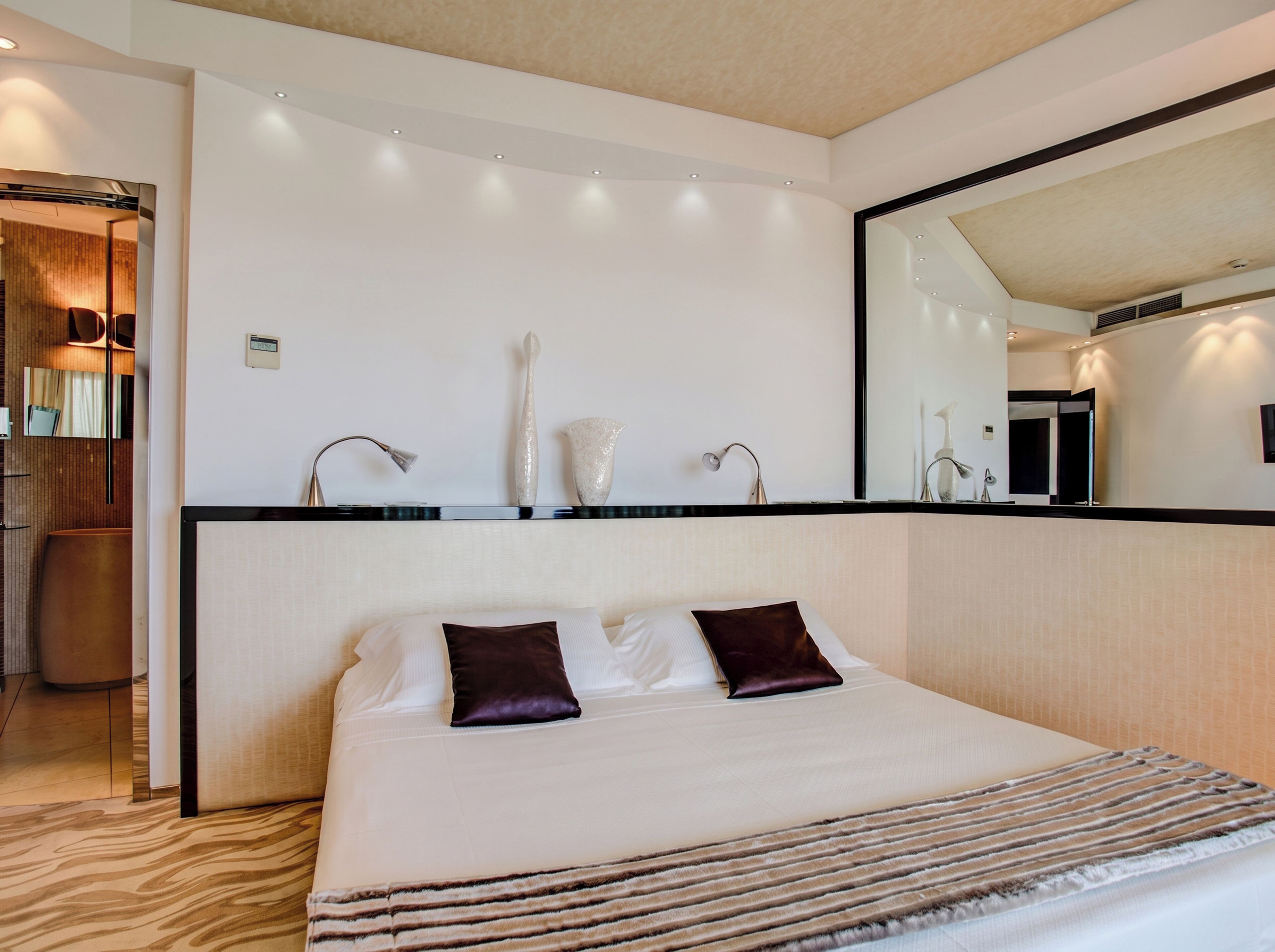 Quarto de hotel com cama grande, mesa de cabeceira, espelho e luminária na parede.
