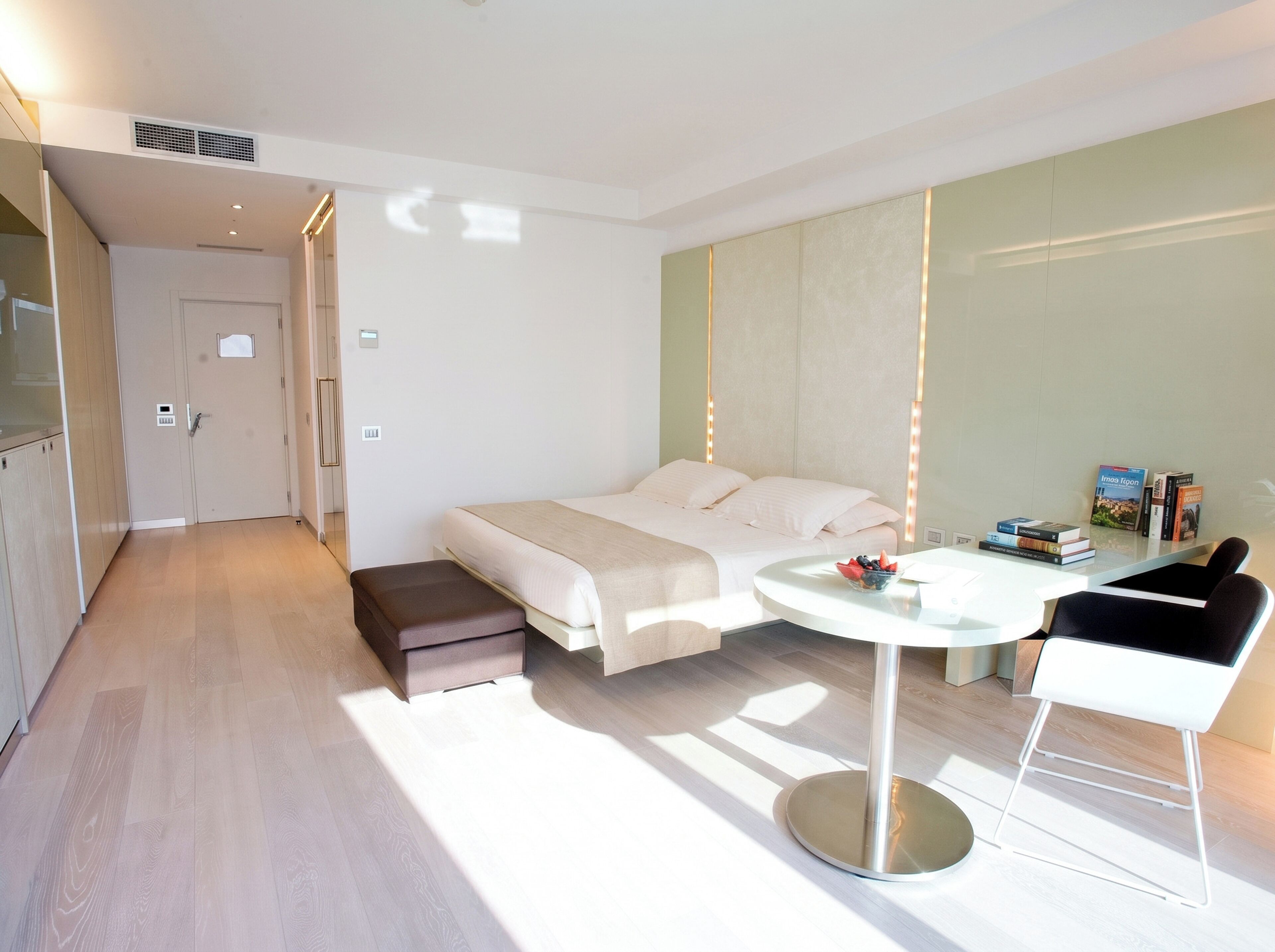 A modern hotel room with a bed, bedside table, and a small seating area.