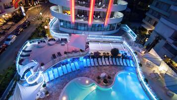 Ein mehrgeschossiges Hotel mit Poolbereich auf dem Dach, inklusive Liegestühlen und Schwimmbecken.