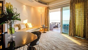 A modern hotel room with a sofa, a dining table, and a balcony with curtains. - Hotel Premier & Suites (Cervia)