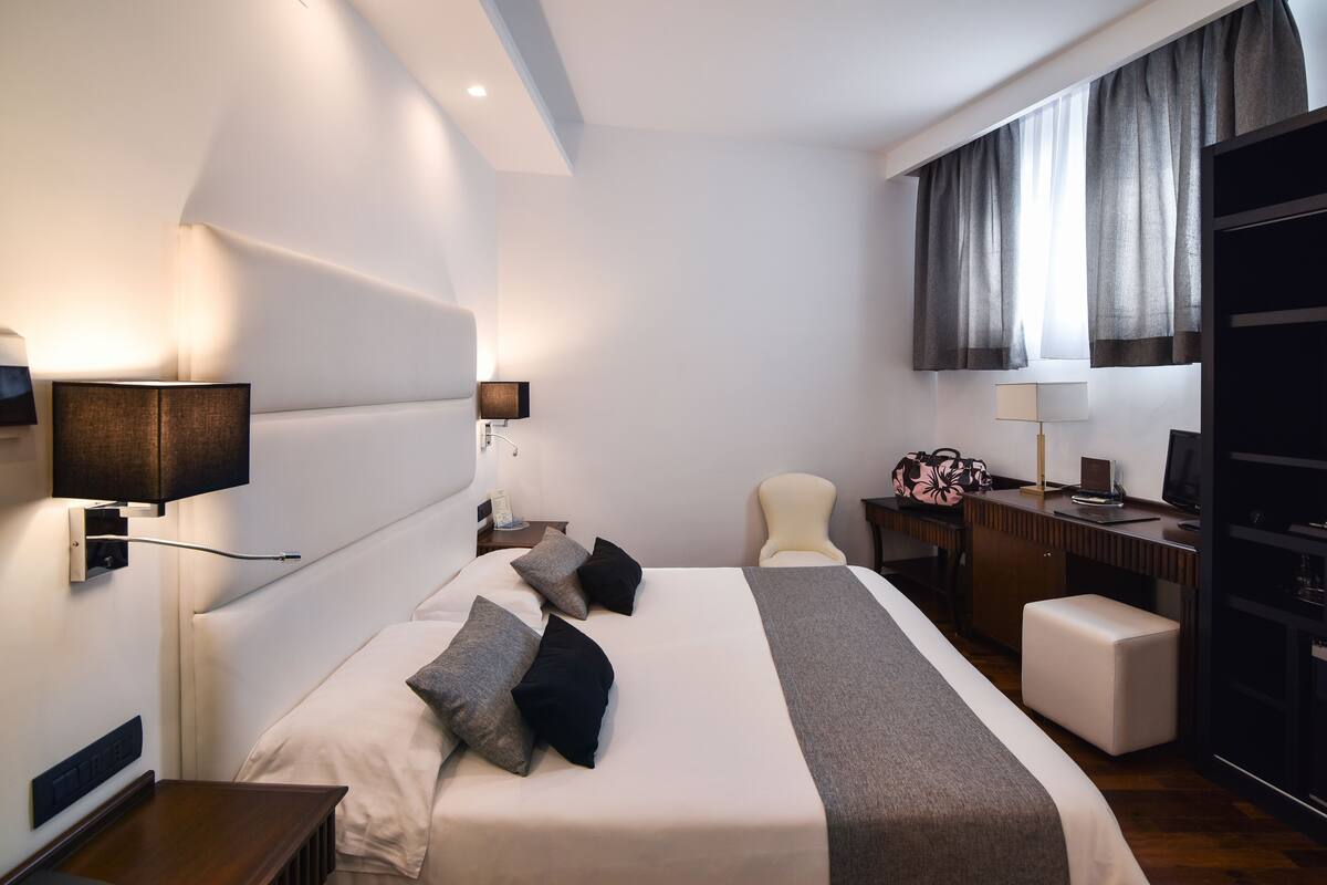 A modern hotel room with a large bed, bedside tables, a desk, and a chair.