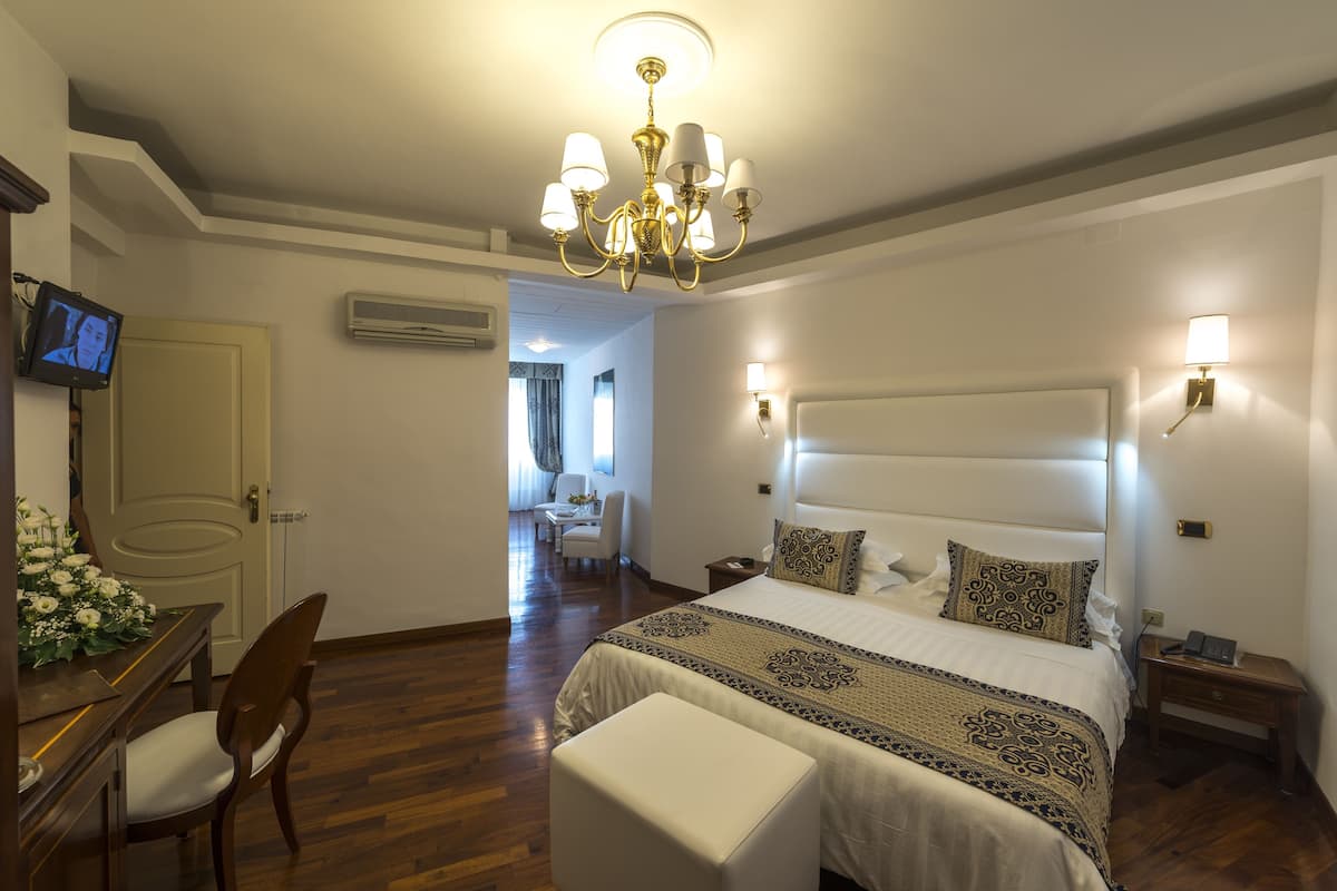 A hotel room with a large bed, a desk with a chair, a television, and a chandelier.