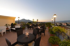 Une terrasse sur le toit, avec des tables et des chaises rondes, des plantes en pot et des lampadaires.