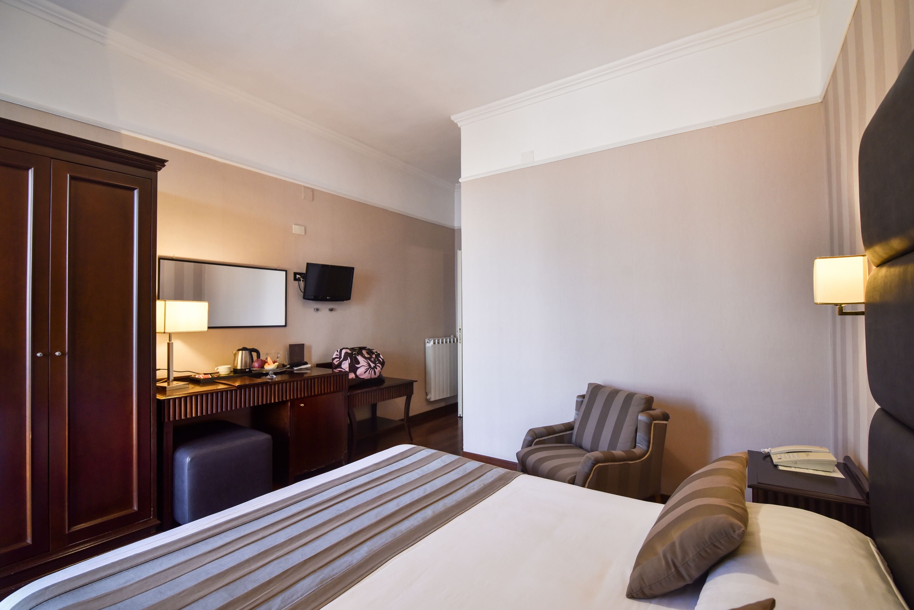 Una habitación de hotel con cama, escritorio, silla, televisor y mesita de noche.