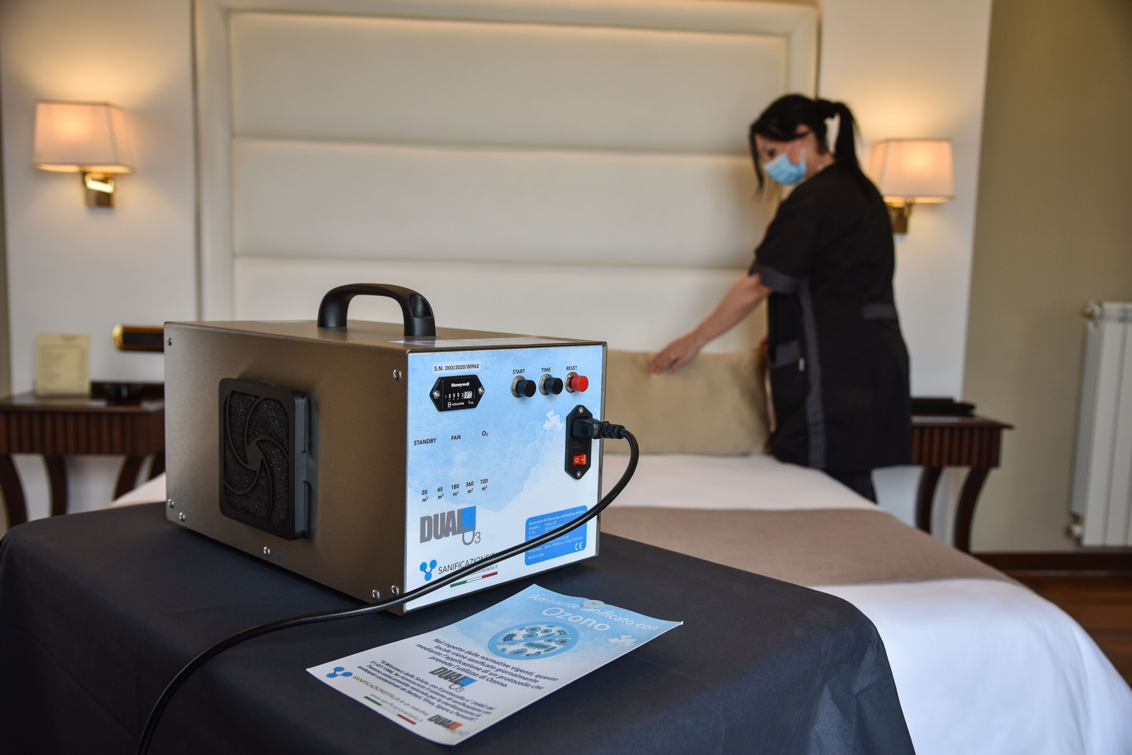 Un dispositivo médico sobre una mesa en una habitación de hotel, con cama y mesitas de noche.