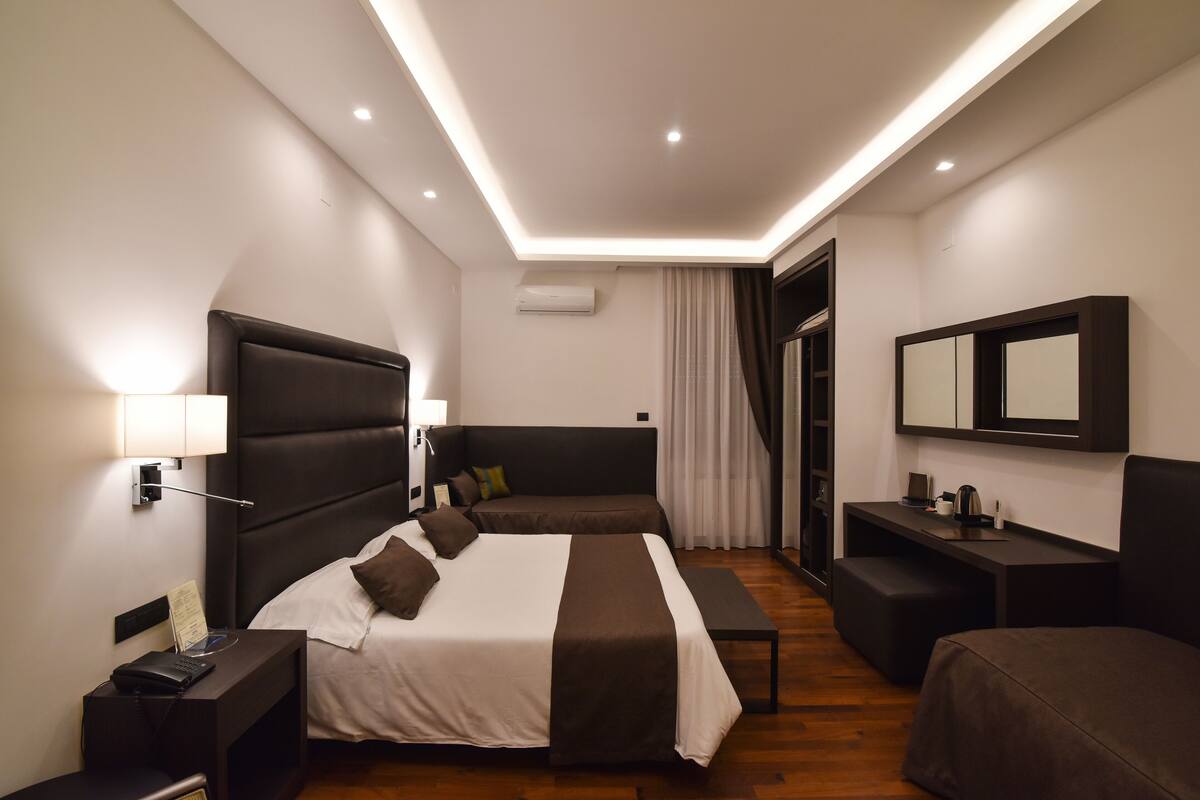A modern hotel room with a large bed, bedside tables, a desk, and a mirror.