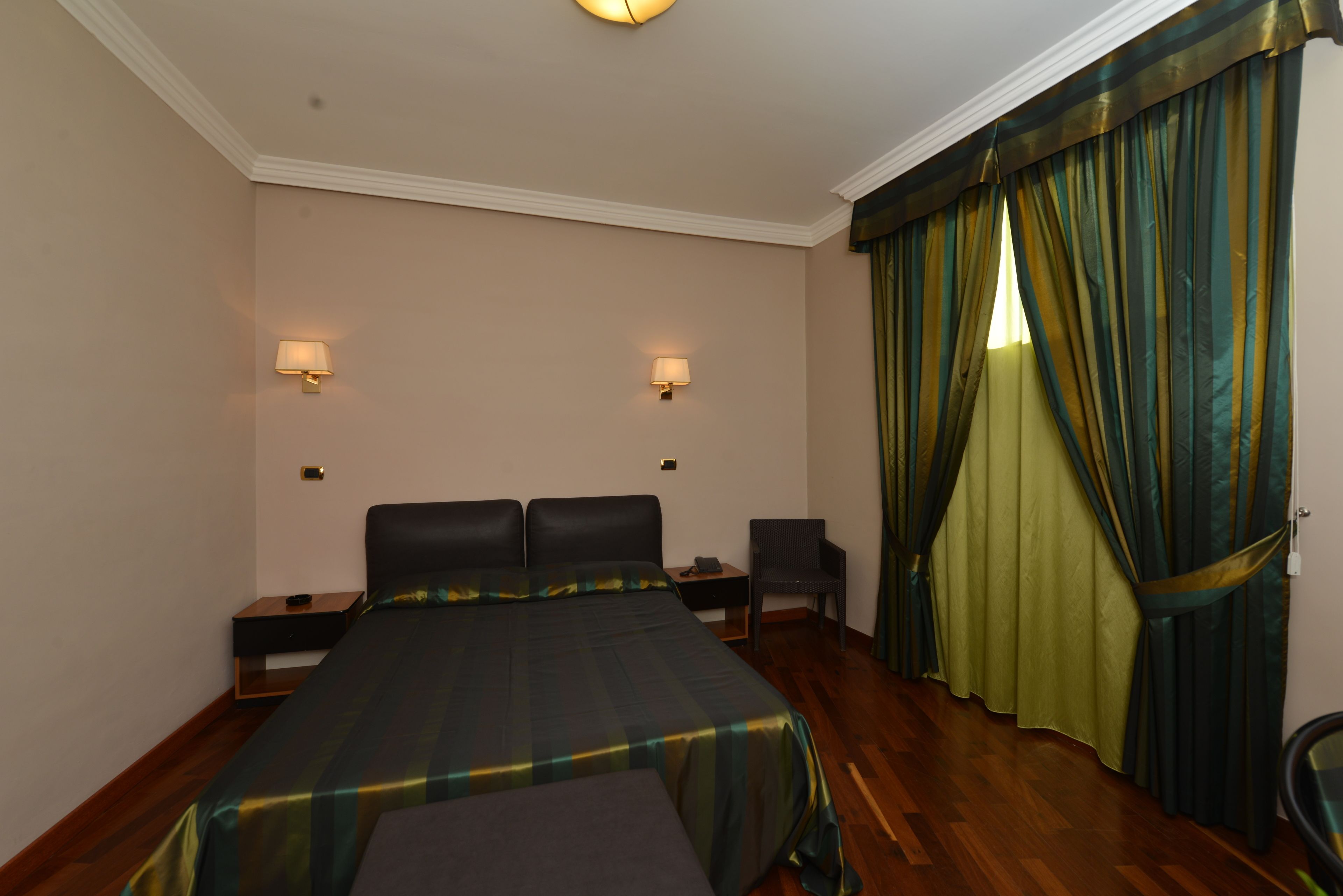 A hotel room with a bed, two nightstands, a chair, and a window with curtains.