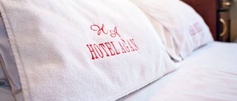 Une chambre d’hôtel avec un lit, un oreiller blanc orné de motifs brodés et une table de chevet en bois.
