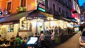 Un immeuble abritant un restaurant appelé « Alute » au rez-de-chaussée, avec une terrasse et une enseigne.