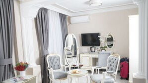 Une chambre d’hôtel avec un grand miroir, une télévision, un bureau avec un ordinateur portable et deux chaises. On y trouve également une petite table avec un plateau en verre et une plante en pot.