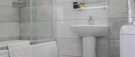 Un baño con ducha de vidrio, lavamanos sobre pedestal y retrete.