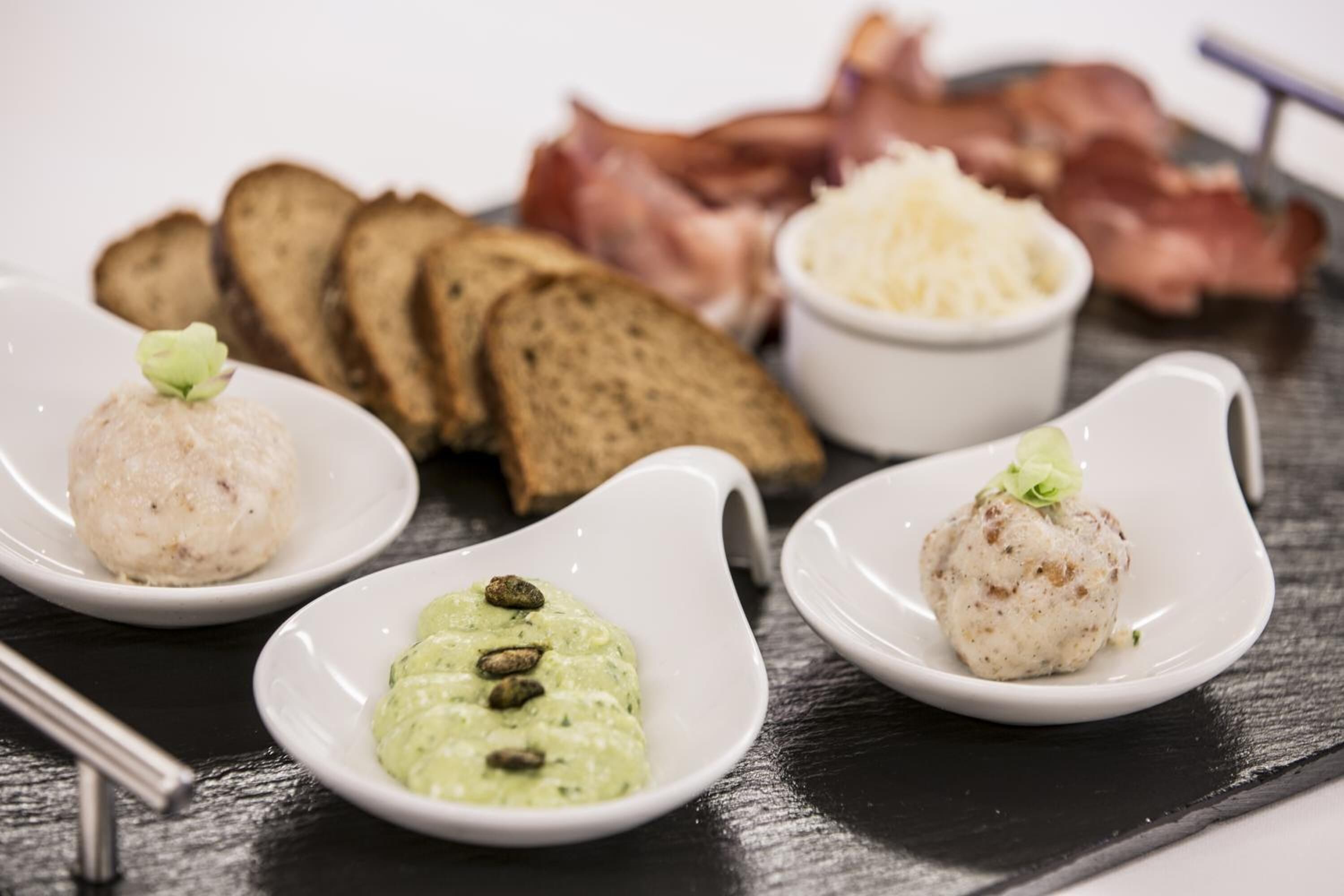 Un plato con tres tazones pequeños de comida, rebanadas de pan y trozos de tocino.