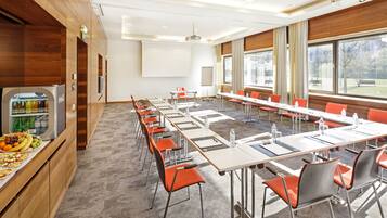 A conference room with long tables, orange chairs, a refrigerator with beverages, and large windows.