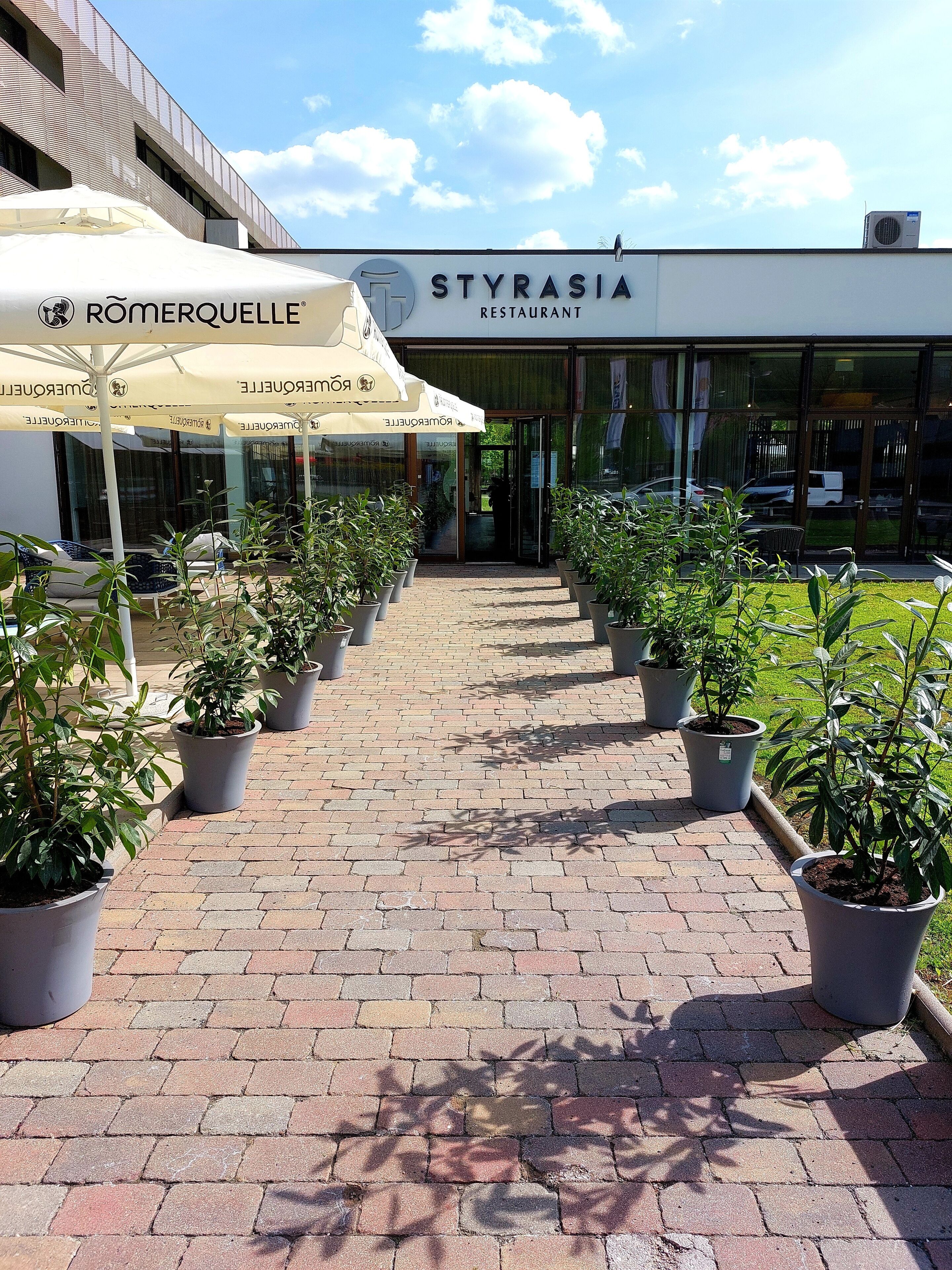 A restaurant named 'STYRASIA' with outdoor seating and potted plants along the walkway.