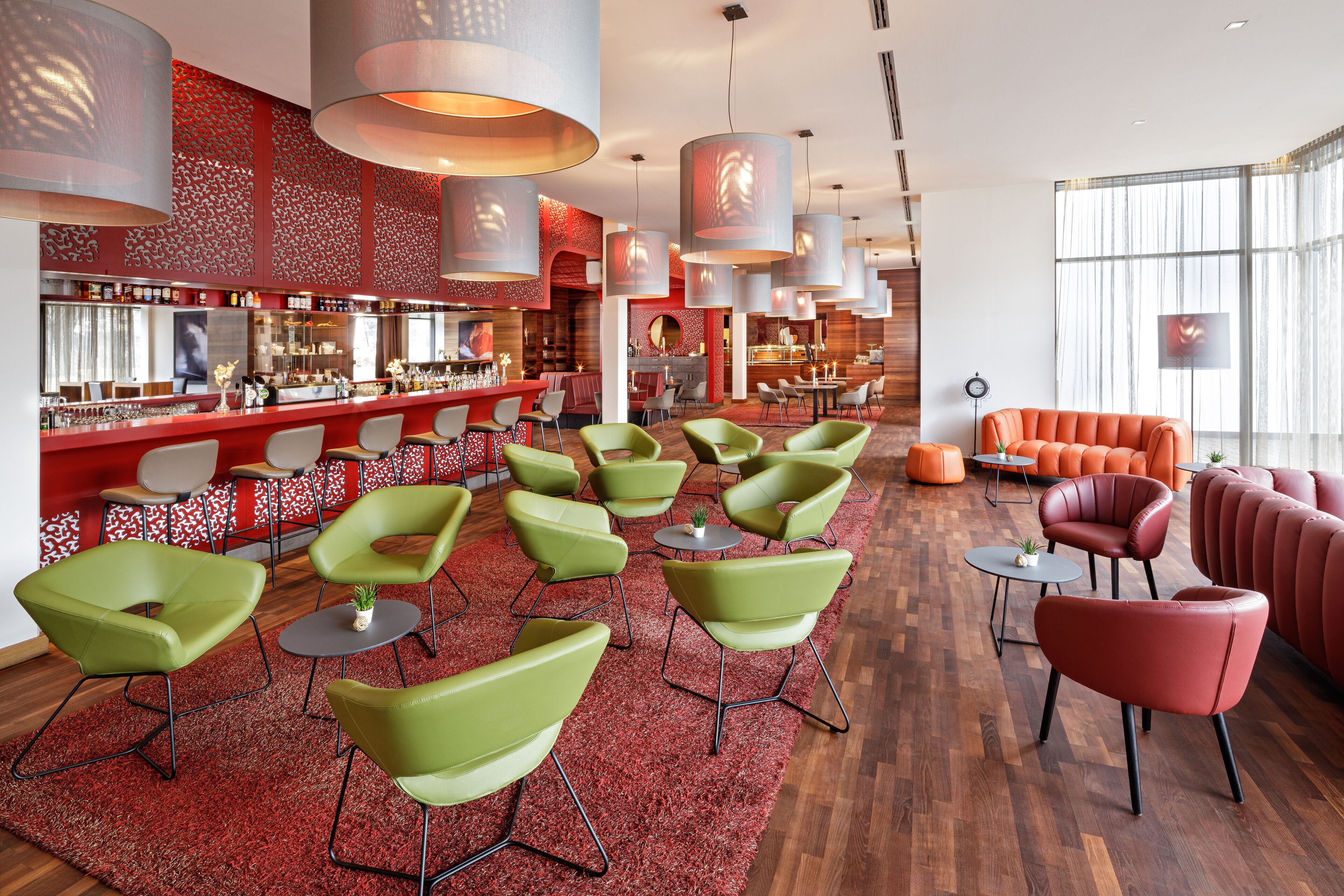 A modern bar area with green and red seating, a bar counter, and large pendant lights.
