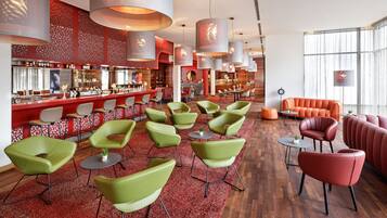A modern bar area with green and red seating, a bar counter, and large pendant lights.