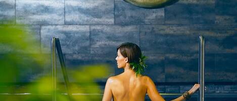 Une personne se trouve dans un spa. On aperçoit un grand bol décoratif accroché au mur, une échelle et une serviette posée sur le sol.