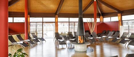A spacious indoor area with a central fire feature, surrounded by rows of lounge chairs.