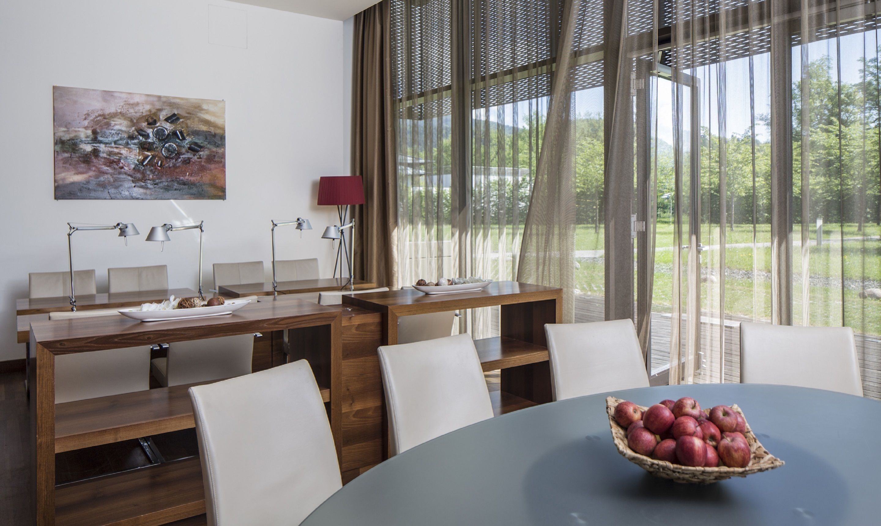 Un espace repas moderne avec une table ronde, des chaises blanches et un banc en bois. Un tableau orne le mur, et une fenêtre est agrémentée de rideaux légers.