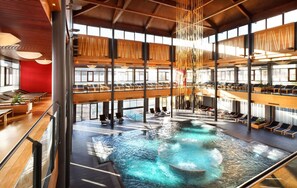 Un amplio espacio interior con piscina que cuenta con varios niveles, zonas de estar y un elemento acuático central.
