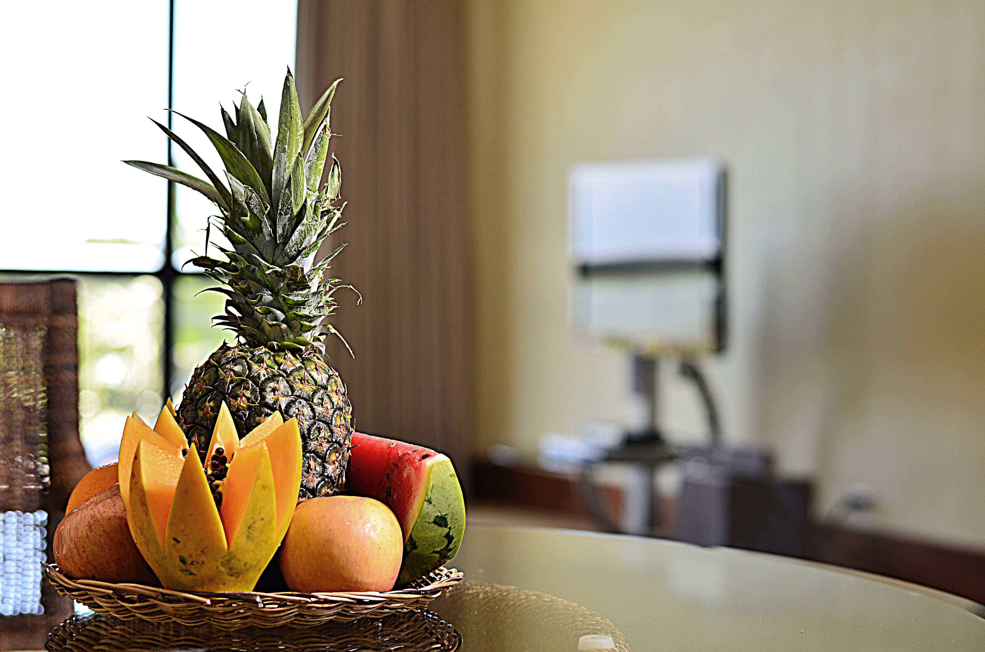 Una cesta de frutas sobre una mesa, con una ventana al fondo.